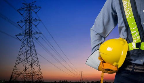 Engineer holding a safety helmet beside a high-voltage transmission tower